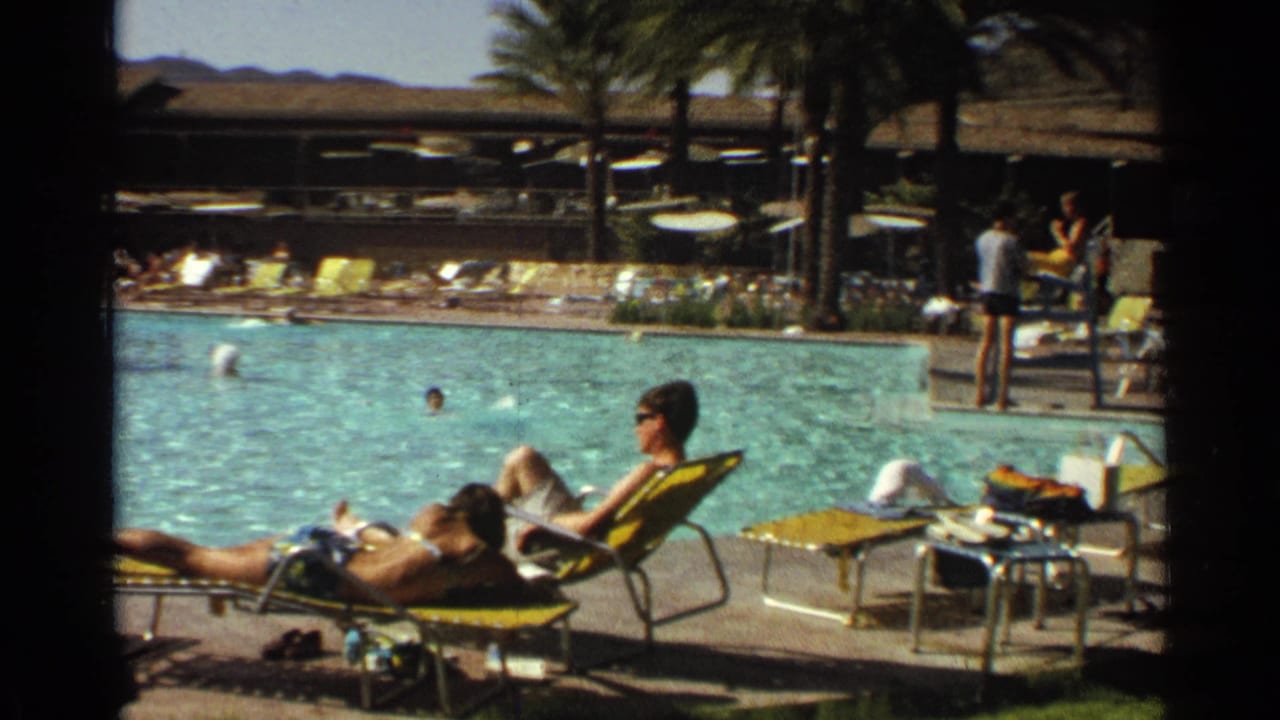 1968 Scottsdale resort pool scene with adults sunbathing on yellow loungers, swimmers in turquoise water, palm trees, and desert hills beyond.