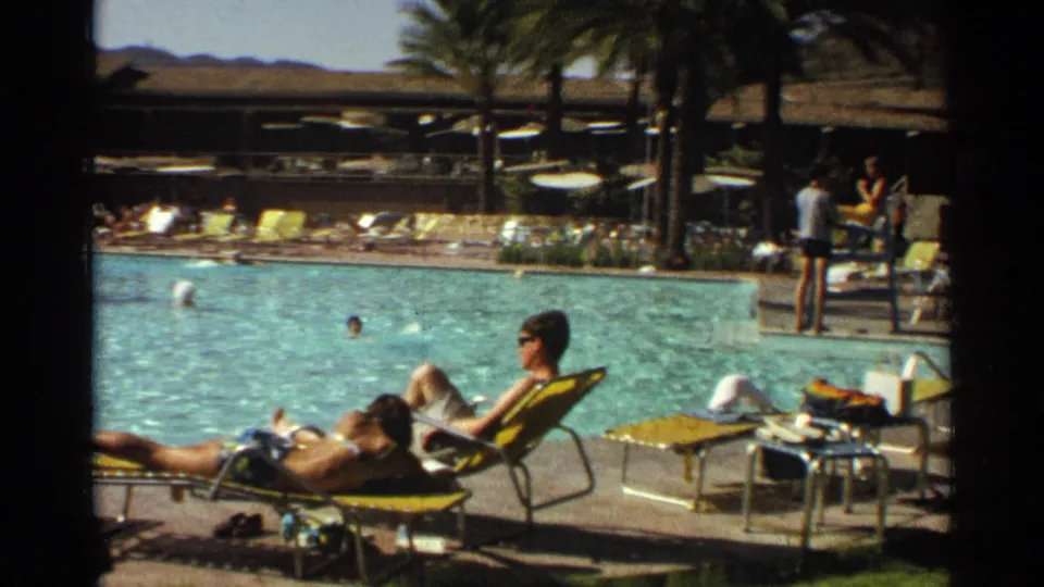 1968 Scottsdale resort pool scene with adults sunbathing on yellow loungers, swimmers in turquoise water, palm trees, and desert hills beyond.