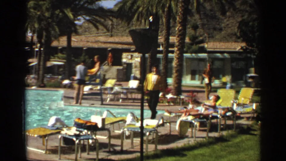 1968 Scottsdale resort pool area with palm trees, lounge chairs, sunbathers, and a man in yellow moving through the scene.