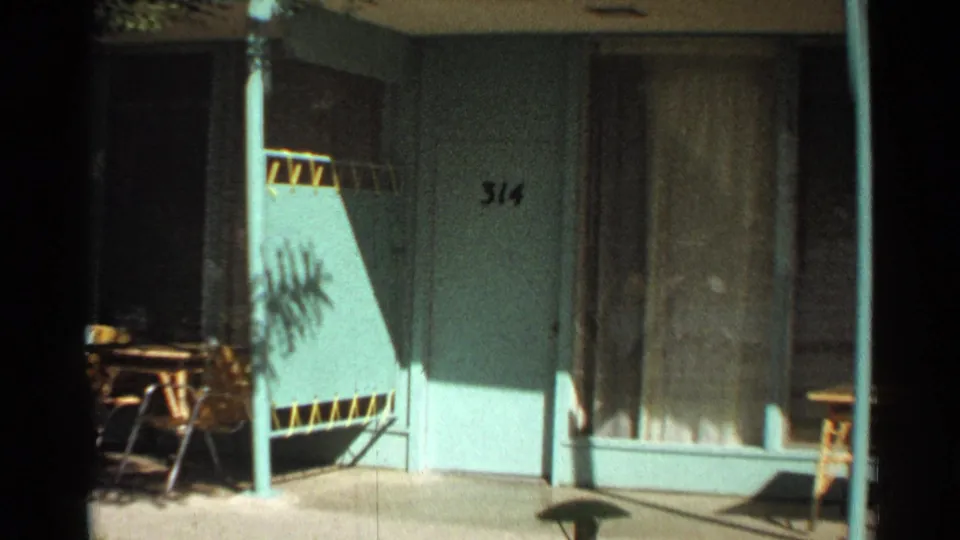 1968 Scottsdale motel exterior detail with turquoise walls, room number 314, curtained window, patio chairs, and strong sunlight.