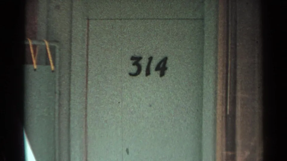 Scottsdale motel exterior detail from 1968 footage, showing a green door marked 314 and a partial patio seat at frame edge.
