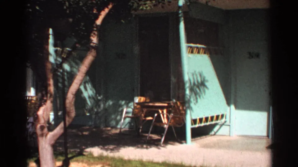 1968 Scottsdale motel courtyard view with a tree trunk in front of green doors and mid-century patio furniture near the walkway.