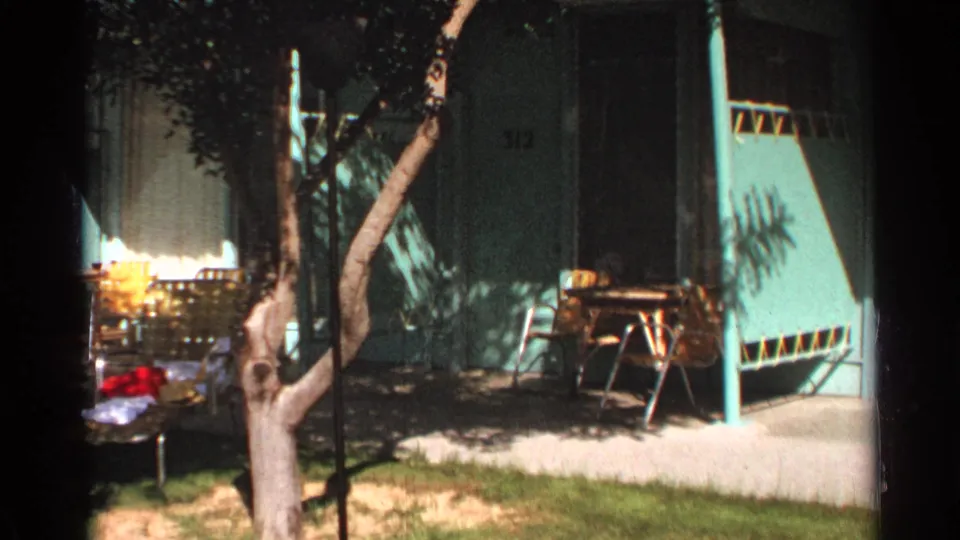 Scottsdale motel courtyard in 1968, with room numbers partly visible, a leaning tree trunk, lawn, walkway, and outdoor seating.