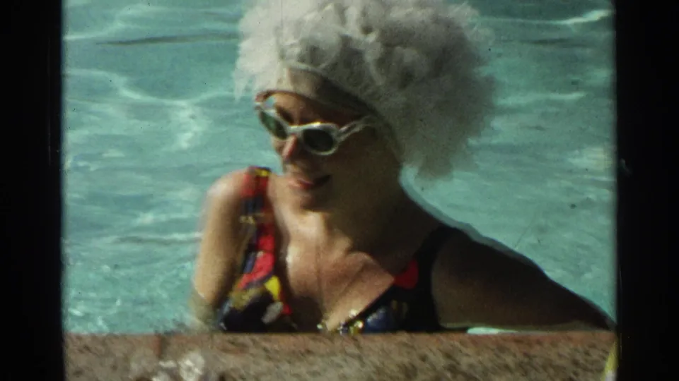 The 1968 Scottsdale home movie shows the woman smiling in the pool, with her white wig, cat-eye sunglasses, and patterned swimsuit visible.