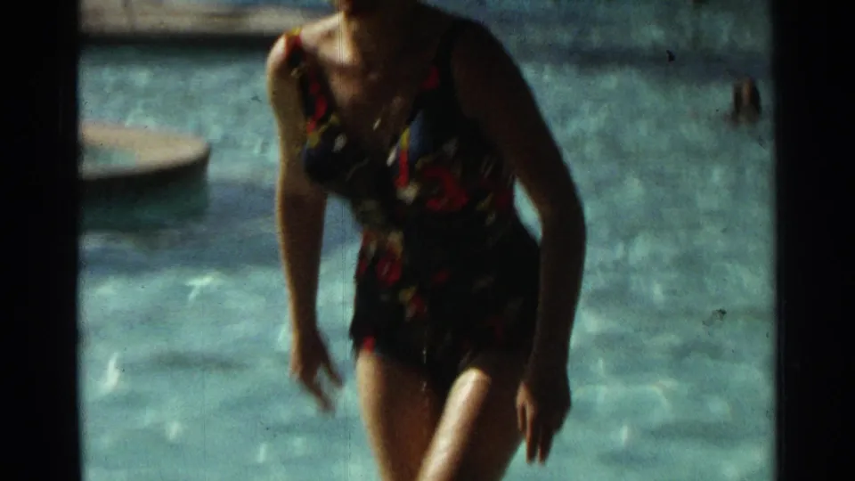 At the end of the 1968 Scottsdale clip, the woman rises from the pool in a patterned swimsuit, with the white wig still visible.