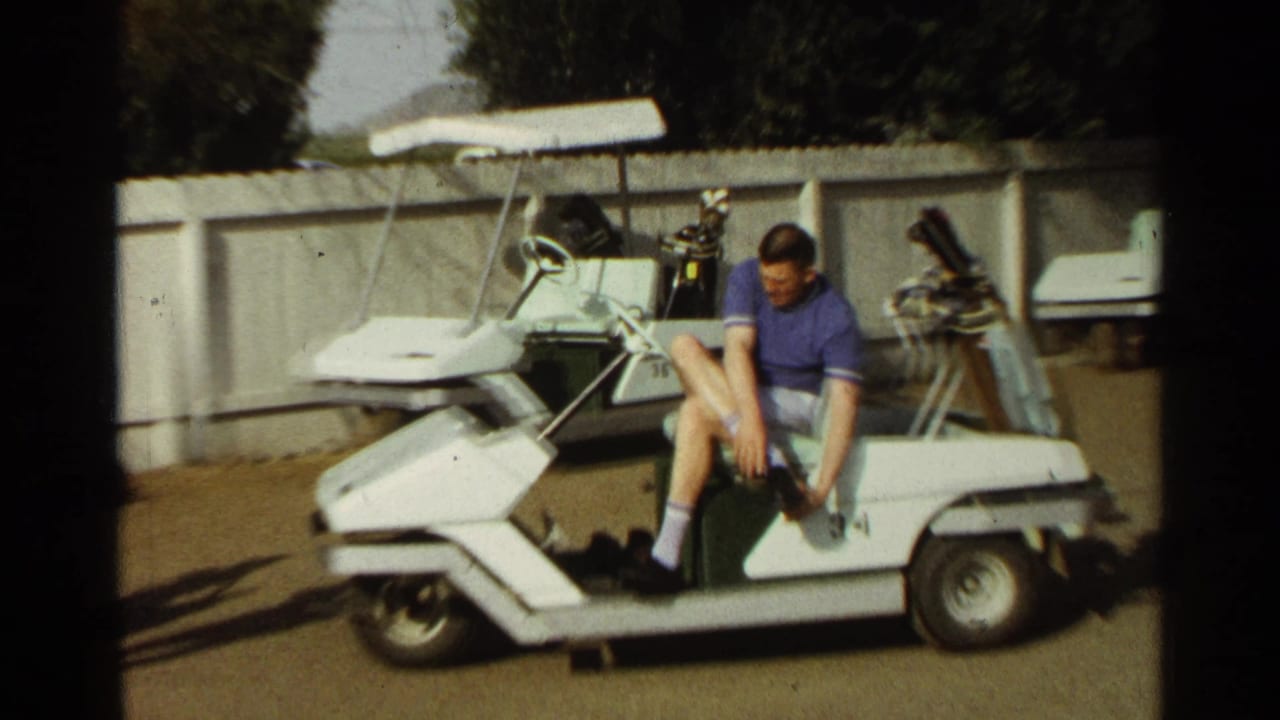 Man sitting on a white golf cart adjusting his shoe near golf clubs.