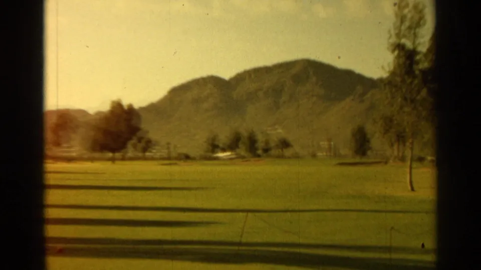 Wide 1968 Scottsdale golf-course view with open green, scattered trees, distant mountains, and warm 8mm exposure.