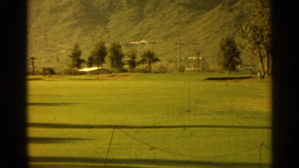 1968 Scottsdale course view showing green fairway, trees, mountain slope, utility poles, and a small sand or bare-ground patch.