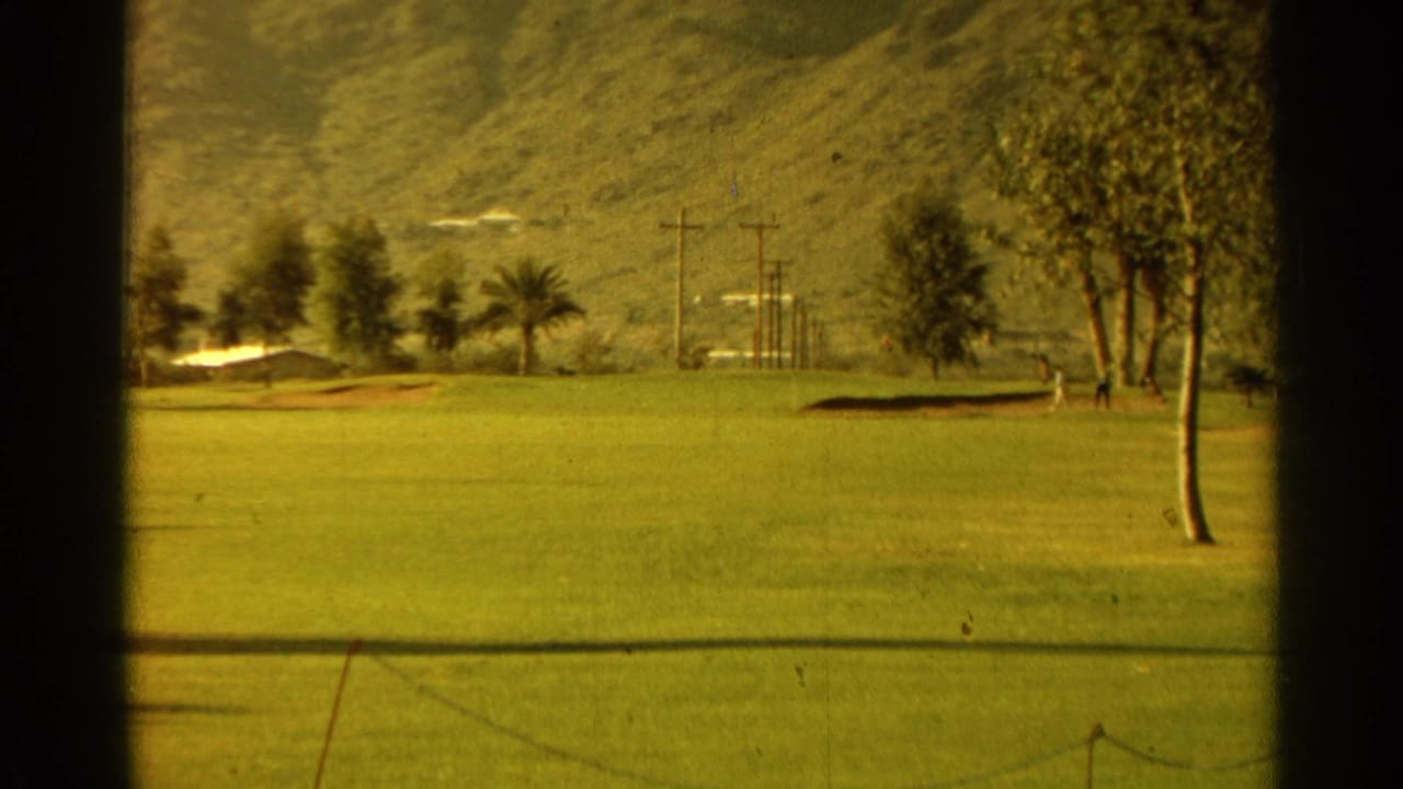 Golf fairway with trees, utility poles, and mountains seen through dark 8mm frame borders.