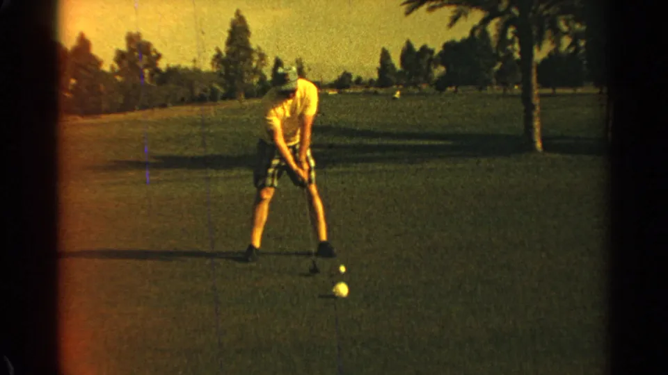 1968 Scottsdale home-movie frame of a golfer in a yellow shirt and plaid shorts preparing a shot on the green.