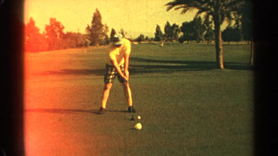 Golfer on a Scottsdale green during a 1968 8mm home movie, with balls, palm trees, and warm light leak visible.