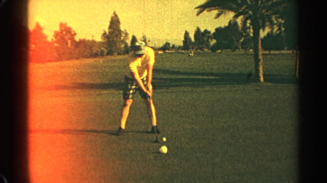 Man in a hat lines up over a golf ball on a sunny course.