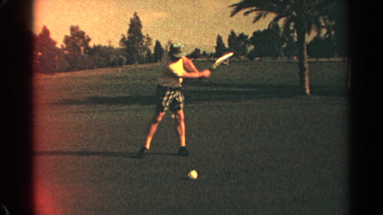 Adult golfer in a yellow shirt prepares a swing on a grassy course.
