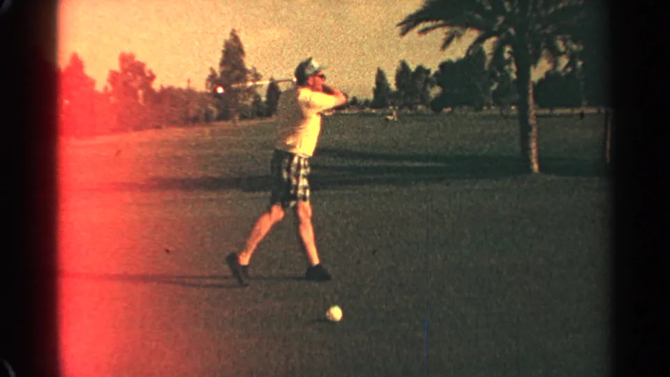 Adult golfer in Scottsdale follows through on a swing, with a golf ball on grass and palm trees in the background.