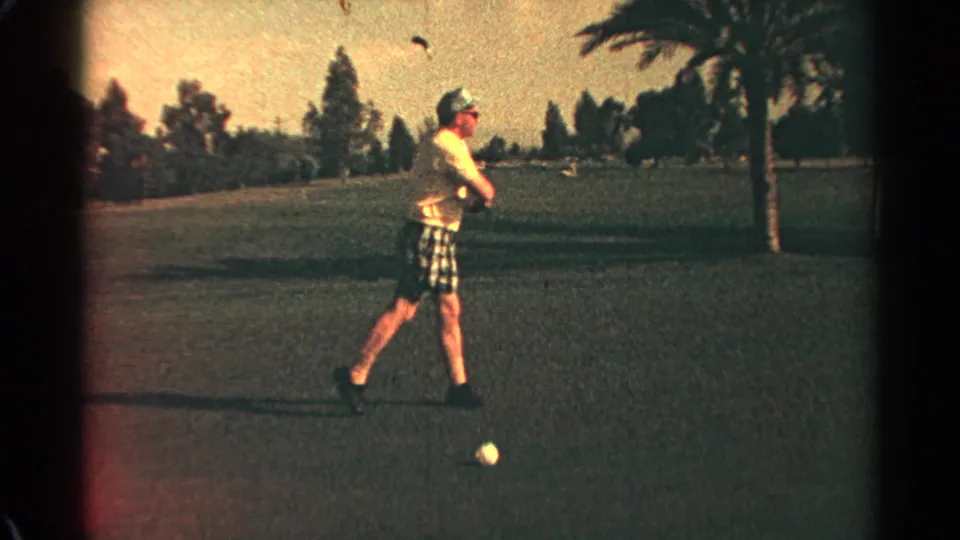 Adult golfer in yellow shirt and plaid shorts lowers his club after swinging on a sunny Scottsdale golf course.