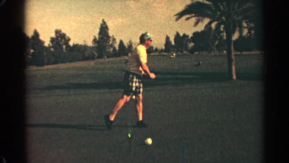 Adult golfer on a 1968 Scottsdale course stands with club lowered near a ball, framed by grass, trees, and a palm.