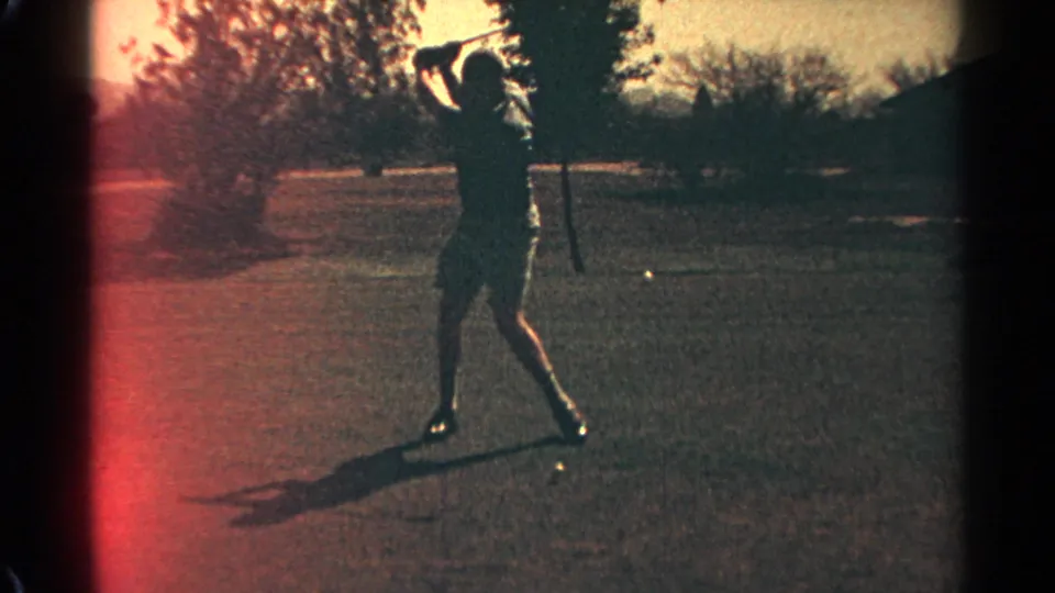 The golfer completes a swing on the Scottsdale course, silhouetted against the fairway with red film flare along the frame edge.