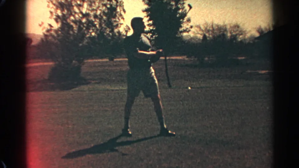 A man in white shorts stands with his golf club on a Scottsdale, Arizona course in 1968, seen through warm, grainy 8mm film.