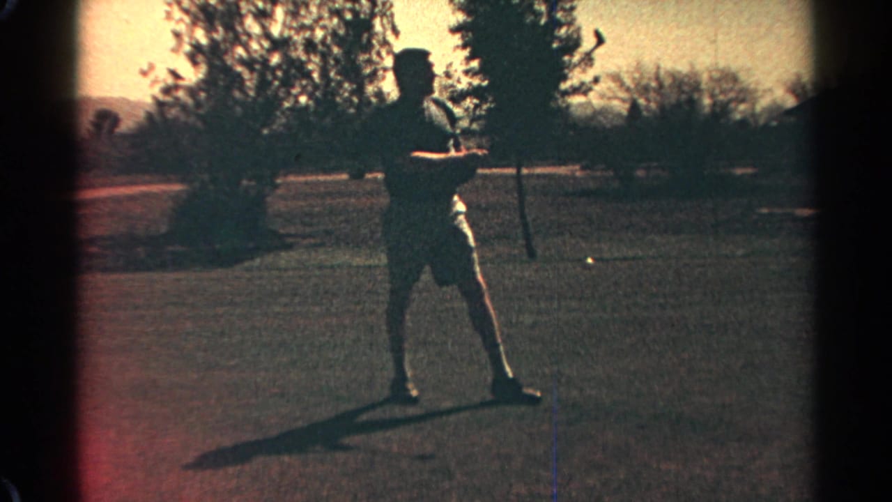 Man standing on a golf course holding a club in warm low light.