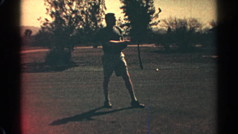 A man on a Scottsdale golf course in 1968 stands with a golf club, framed in soft 8mm color with trees and distant hills behind him.