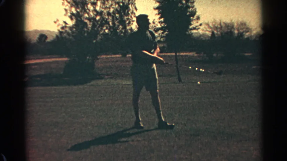 The golfer remains on the Scottsdale course, holding his club near a golf ball as late-day light silhouettes his figure against trees.