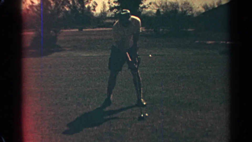 The golfer is seen over the ball in a darker 8mm frame, with grass, trees, and warm Scottsdale course light visible around him.