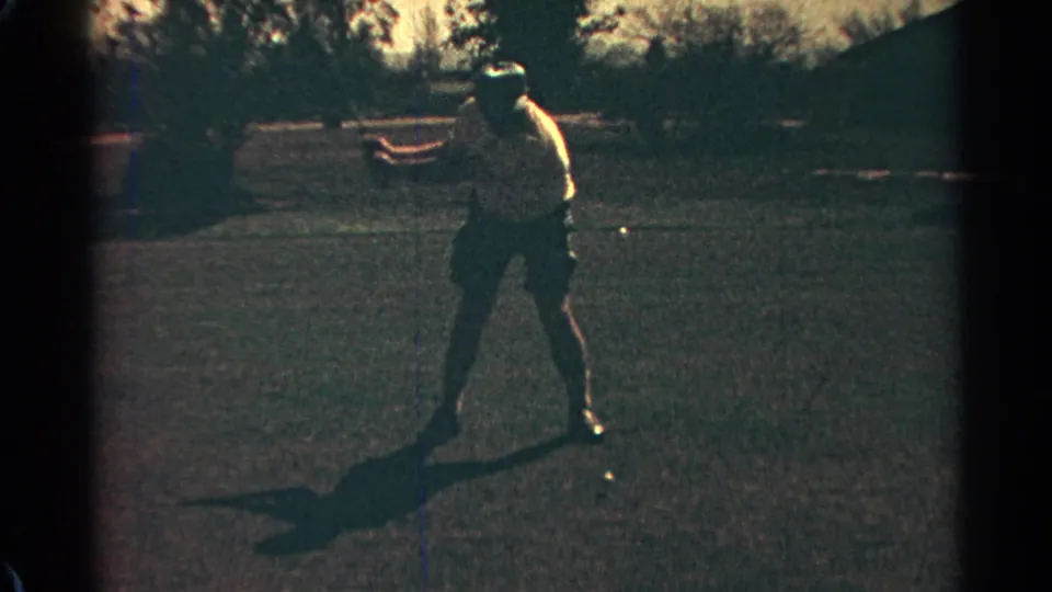 The golfer moves into the early part of his swing, backlit on a Scottsdale grass range in 1968 8mm footage.
