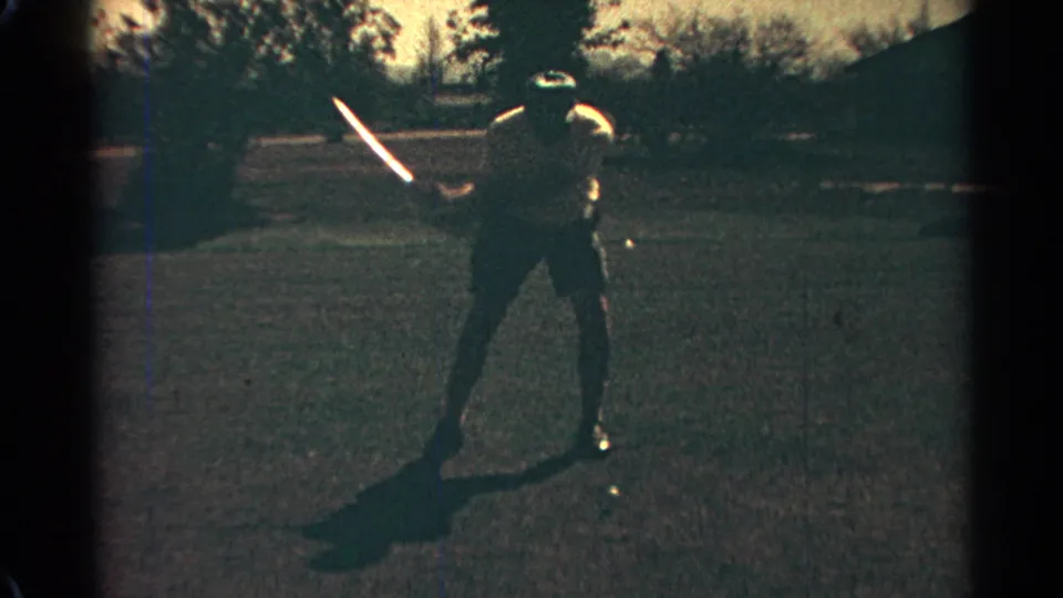 A man reaches the upper part of a golf backswing, silhouetted by strong sunlight in 1968 Scottsdale home-movie footage.
