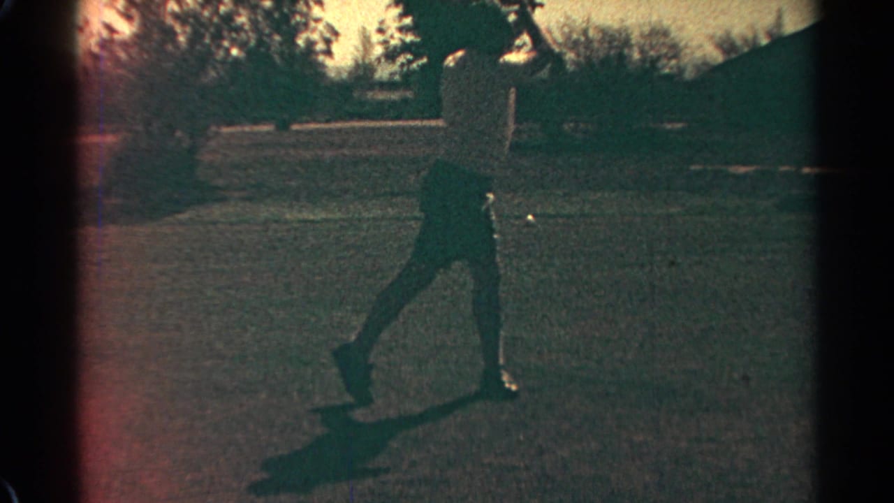 Man on a sunlit golf course beginning a downswing with trees behind him.