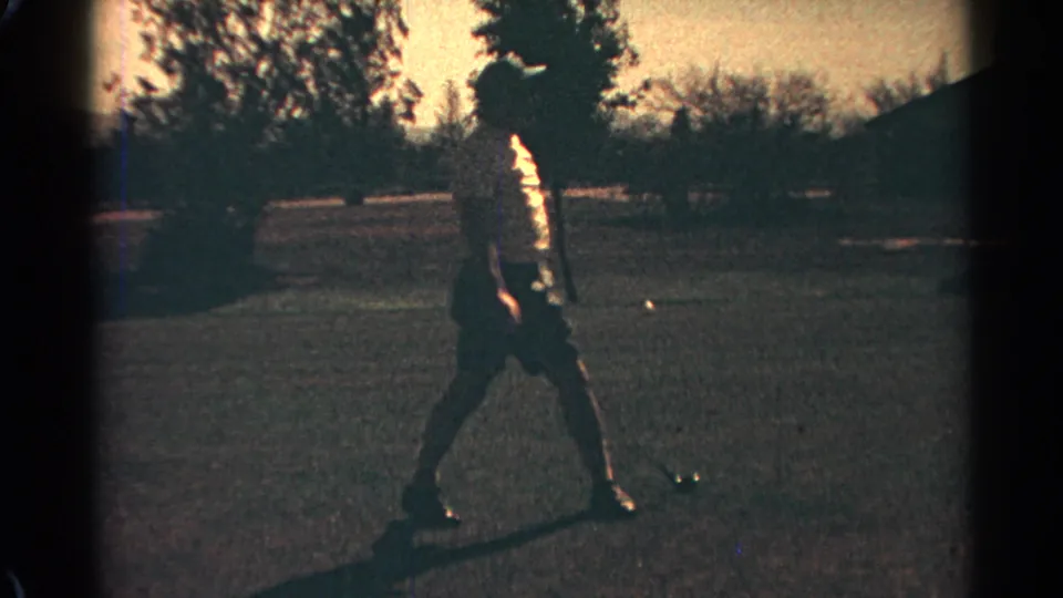 Scottsdale 1968 home-movie still of a golfer finishing a swing, with grass, trees, shadows, and visible 8mm frame edges.