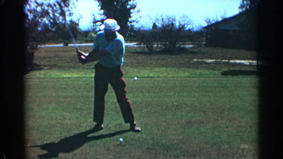 An adult golfer in a white hat starts a club swing on a sunny Scottsdale course, with a golf ball visible on the grass.