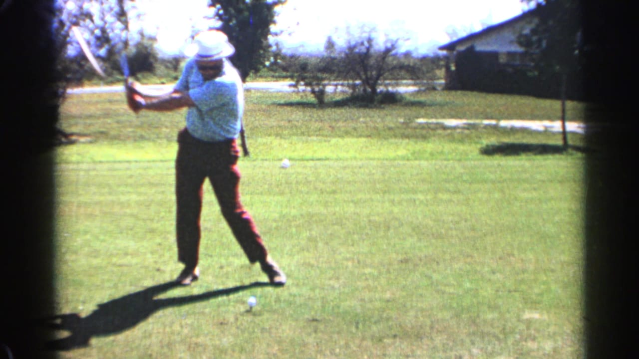 Golfer in a white hat begins a swing on a sunny grassy lawn.