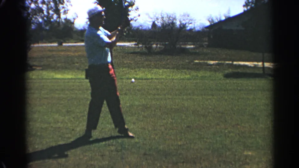 In 1968 Scottsdale, the golfer stands after the drive with the club lowered and a white ball visible on the grass.