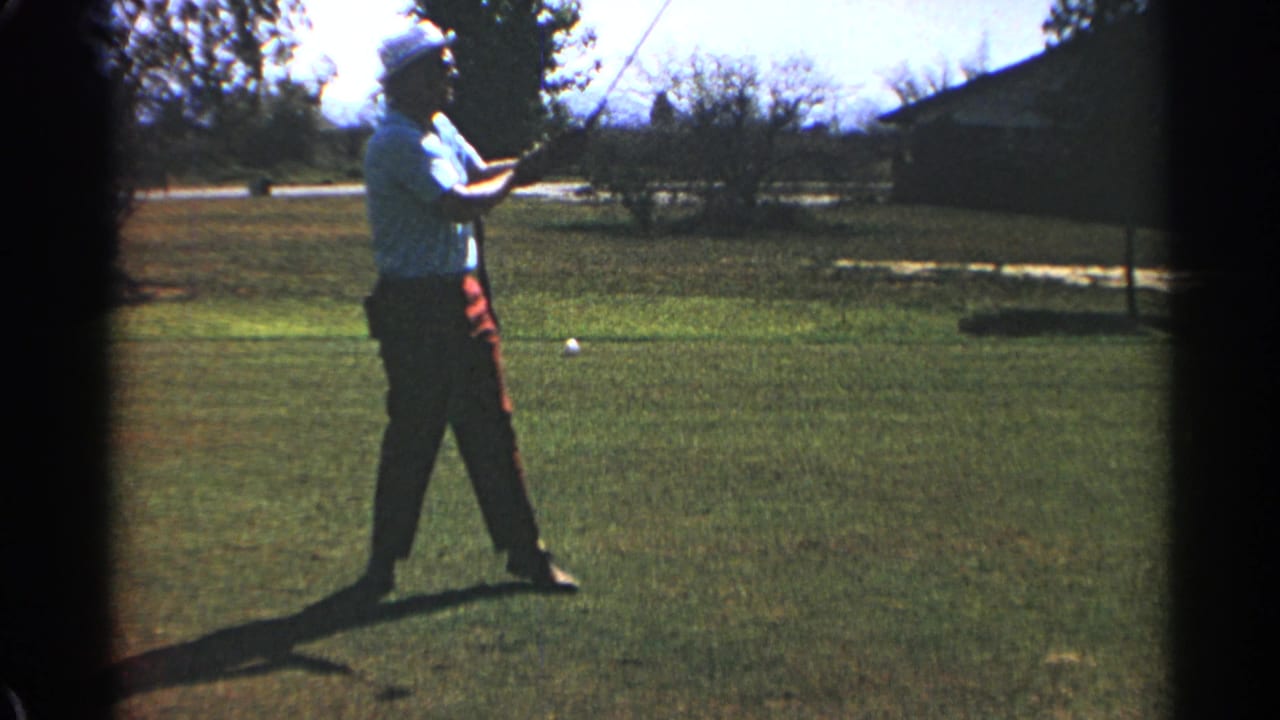 Adult golfer in a white hat finishes a swing on a sunny grass course.