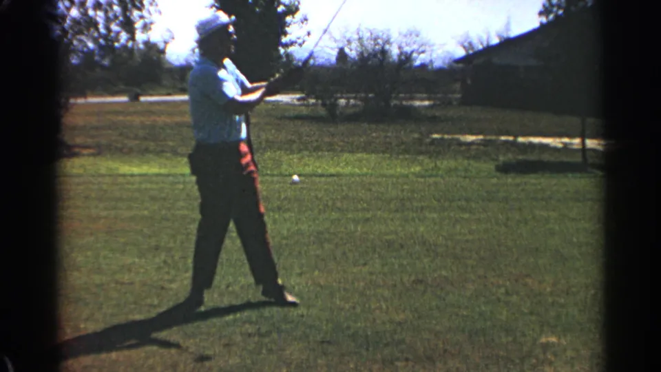 In Scottsdale, Arizona, in 1968, an adult golfer in a light shirt and red trousers follows through on a sunny grass course.