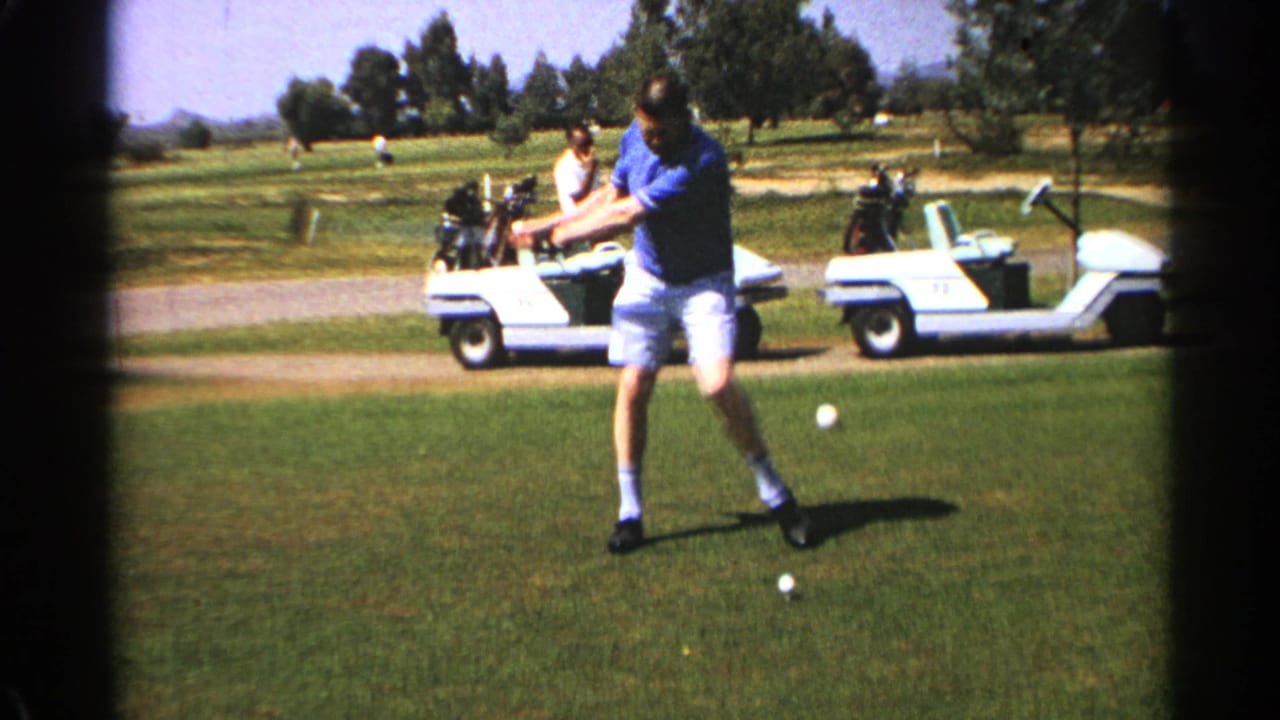 Man in a blue polo prepares to swing a golf club on a sunny course.