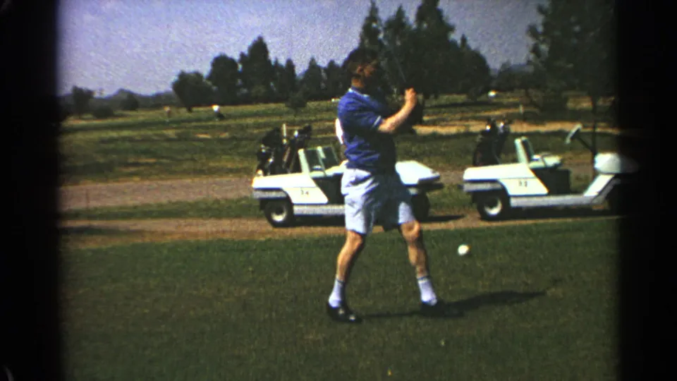 The golfer stands on the tee after a swing in Scottsdale, Arizona, with white golf carts, trees, and distant hills in view.