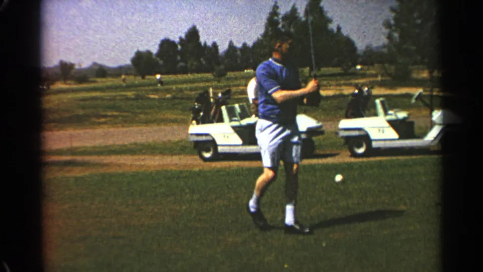 The Scottsdale golf-course view shows the man after his swing, standing near a ball with two white carts behind him.