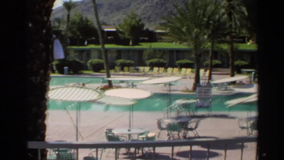 Scottsdale pool area in 1968 with umbrella-shaded tables, palm trees, lounge chairs, and low motel-style buildings near distant hills.