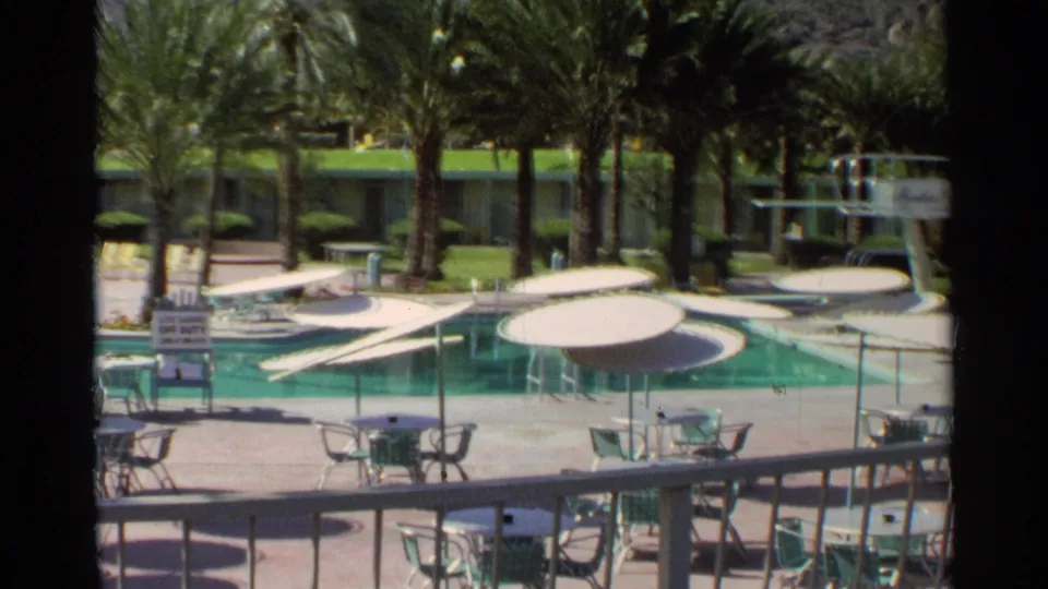 1968 Scottsdale resort pool area with palm trees, green lawn, white umbrellas, patio seating, and a small poolside sign.
