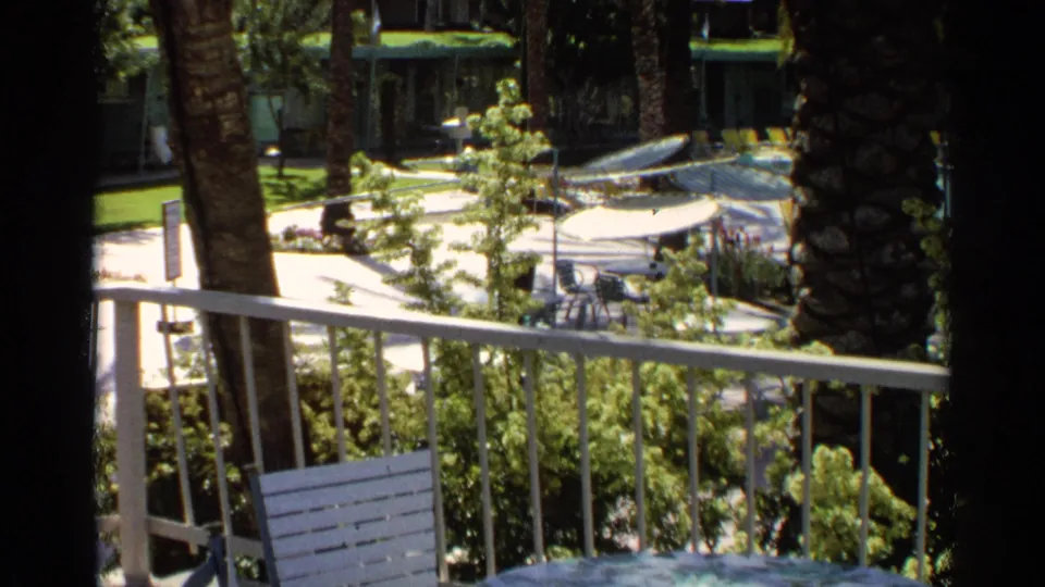 1968 Scottsdale balcony perspective over a landscaped pool area with railing, palms, shrubs, white umbrellas, and diving boards.