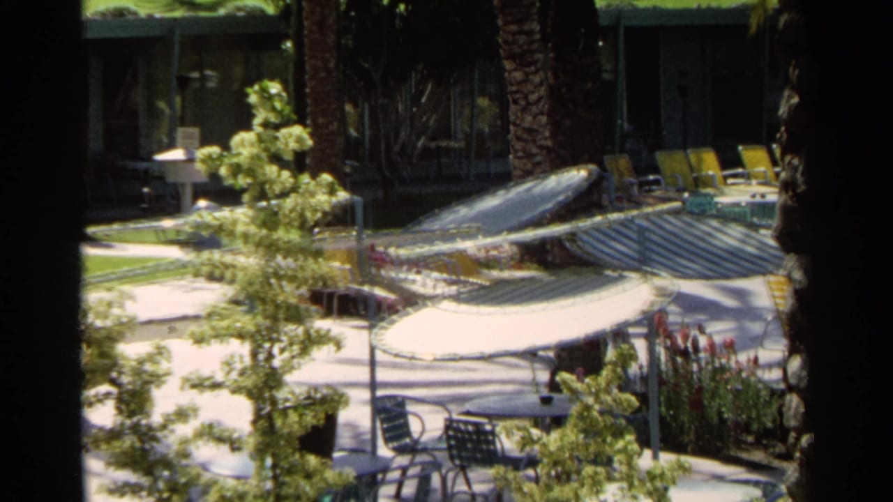 1968 Scottsdale balcony view over a motel pool area with striped umbrellas, yellow lounge chairs, palms, and guests in the distance.