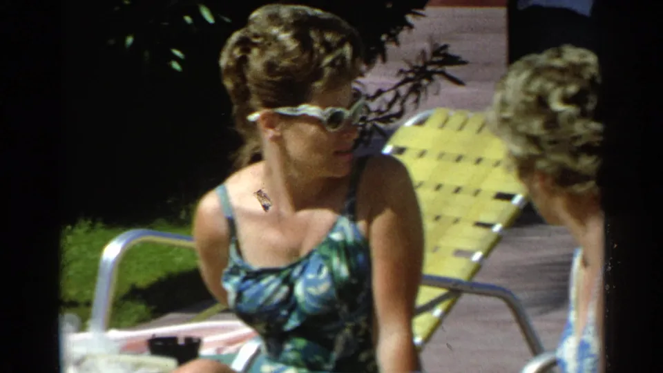 In 1968 Scottsdale poolside footage, a woman in white sunglasses and a patterned swimsuit sits near a yellow lounge chair.
