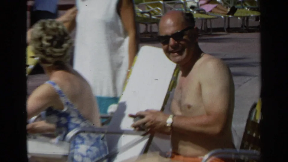 A man in dark sunglasses laughs beside a seated woman at a sunny 1968 Scottsdale poolside setting.
