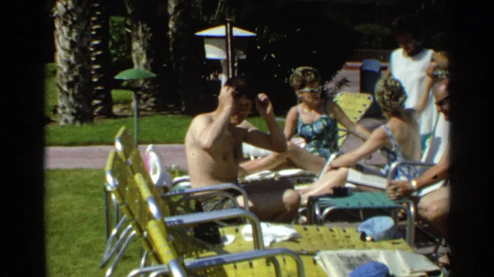 1968 Scottsdale poolside home-movie frame with adults lounging and a shirtless man adjusting his hair or sunglasses.