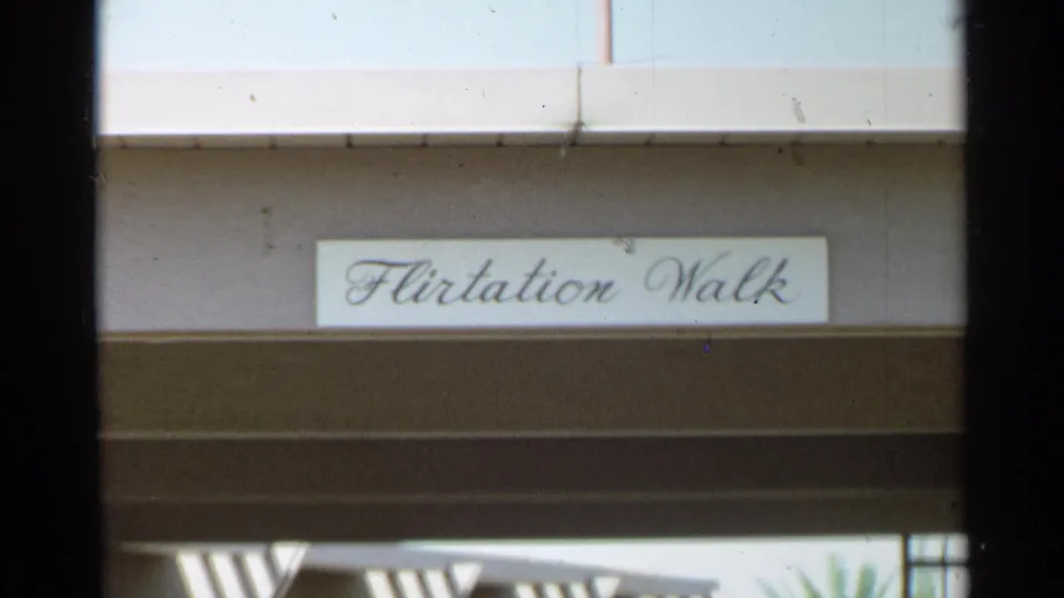 The Flirtation Walk sign remains centered on a resort-style exterior wall, with shaded beams below.