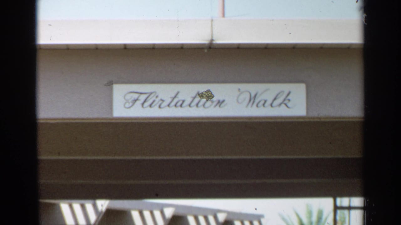 Script sign reading Flirtation Walk on a shaded building facade.
