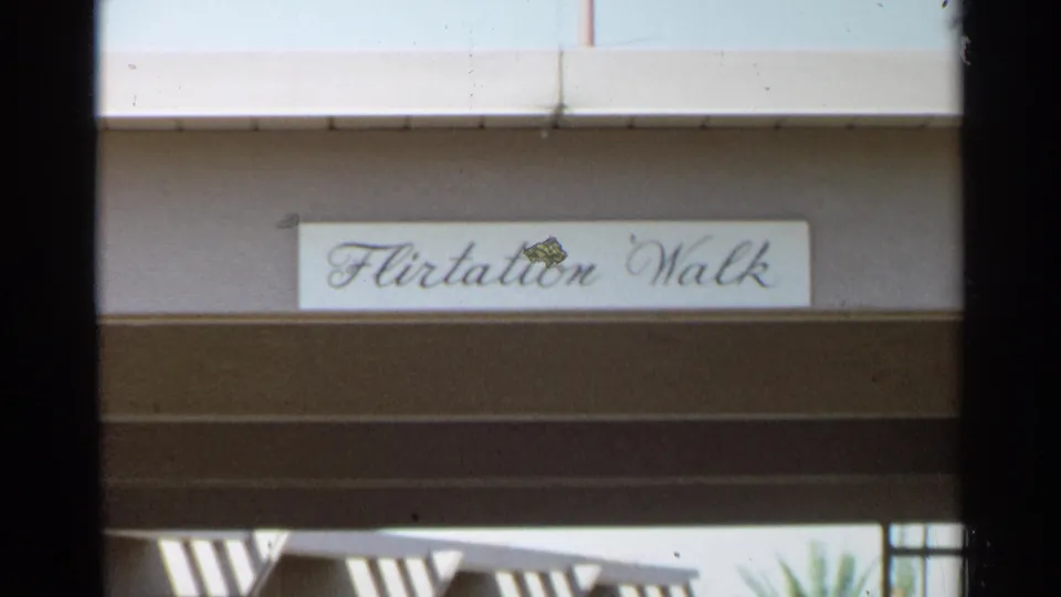1968 Scottsdale home-movie frame showing a Flirtation Walk sign above a shaded mid-century exterior.
