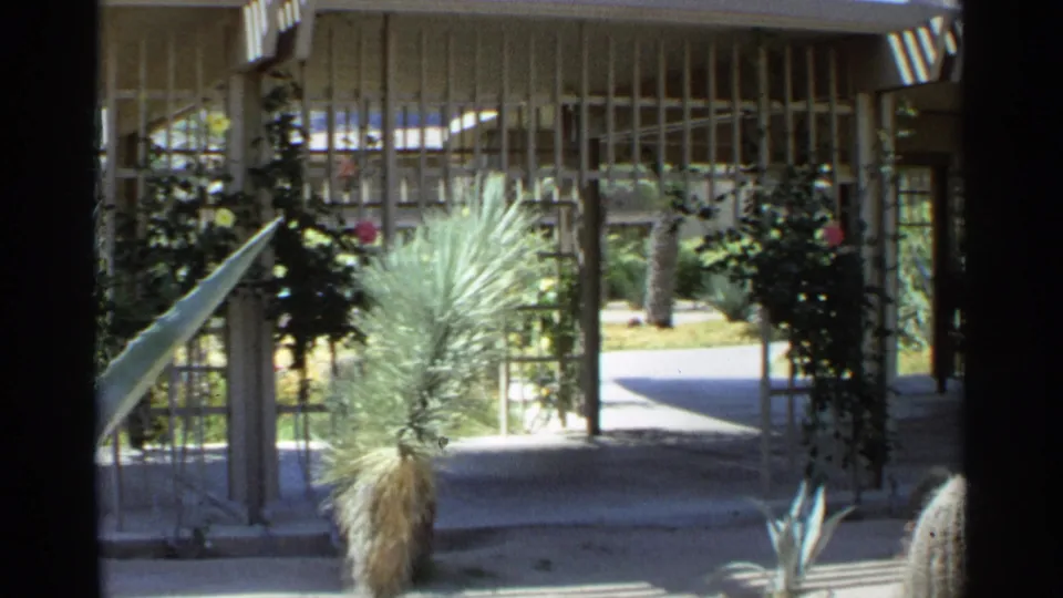 1968 Scottsdale home-movie frame of a shaded courtyard path with desert landscaping and mid-century screening.