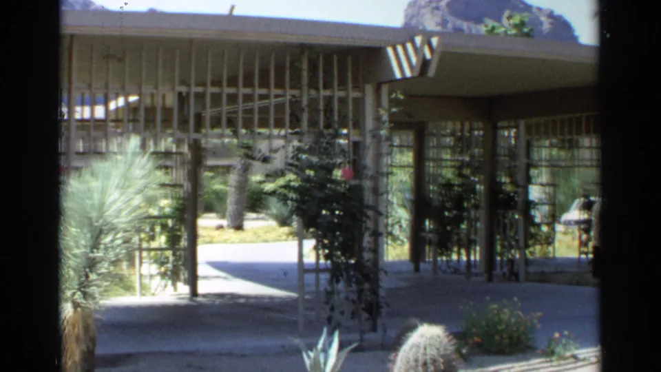 1968 Scottsdale exterior view of a mid-century modern covered entrance framed by cacti, yucca, vines, and a rocky desert backdrop.
